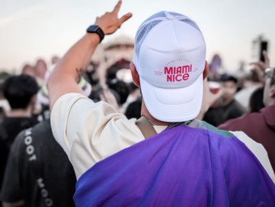 Festivalgast mit weißer Miami-Nice-Cap reckt die Hand in die Luft