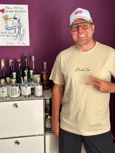 Lachender Mann mit Miami-Nice-Cap und Niced-Tea-Shirt vor einer Hausbar